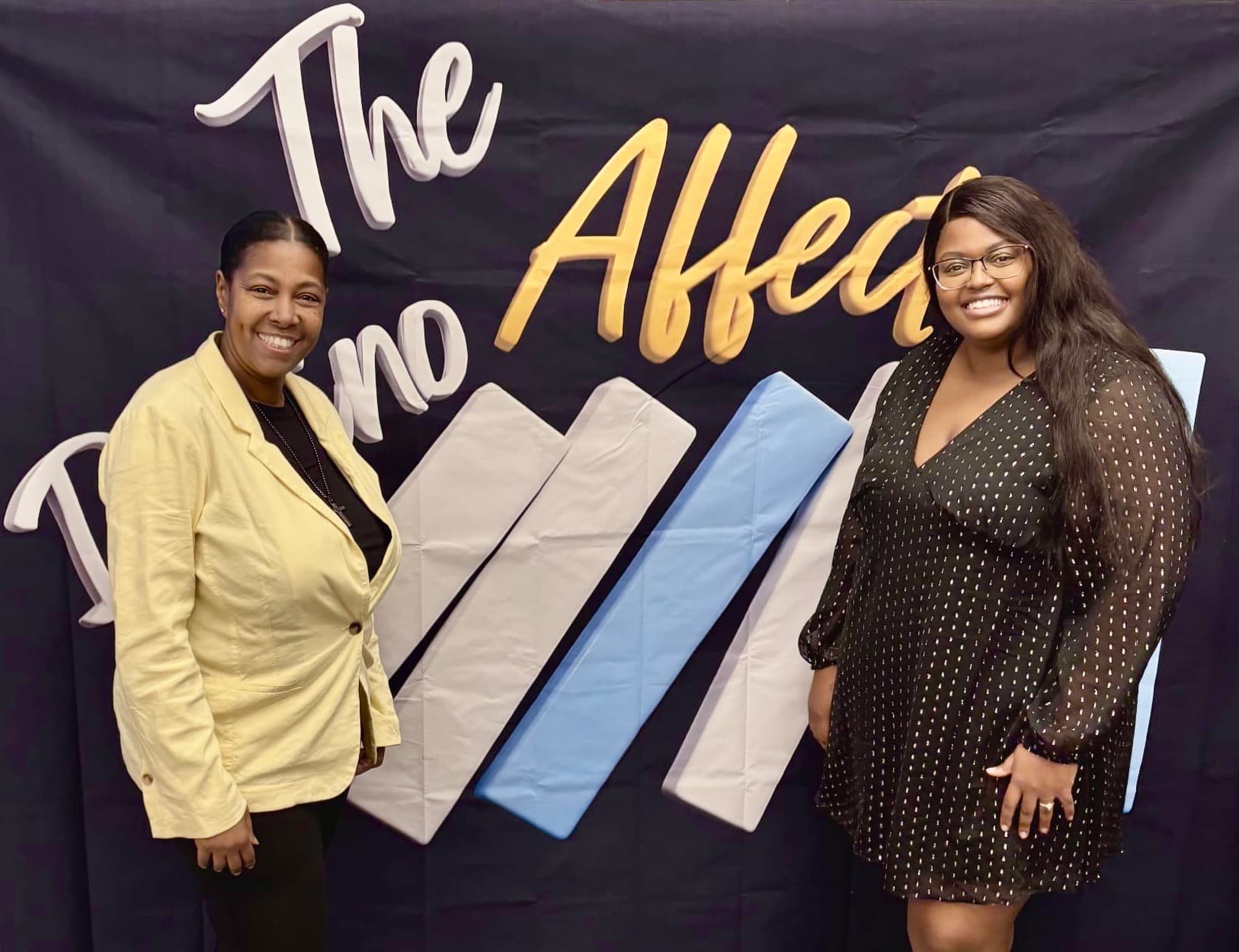 Two women standing in front of The Domino Affect event backdrop